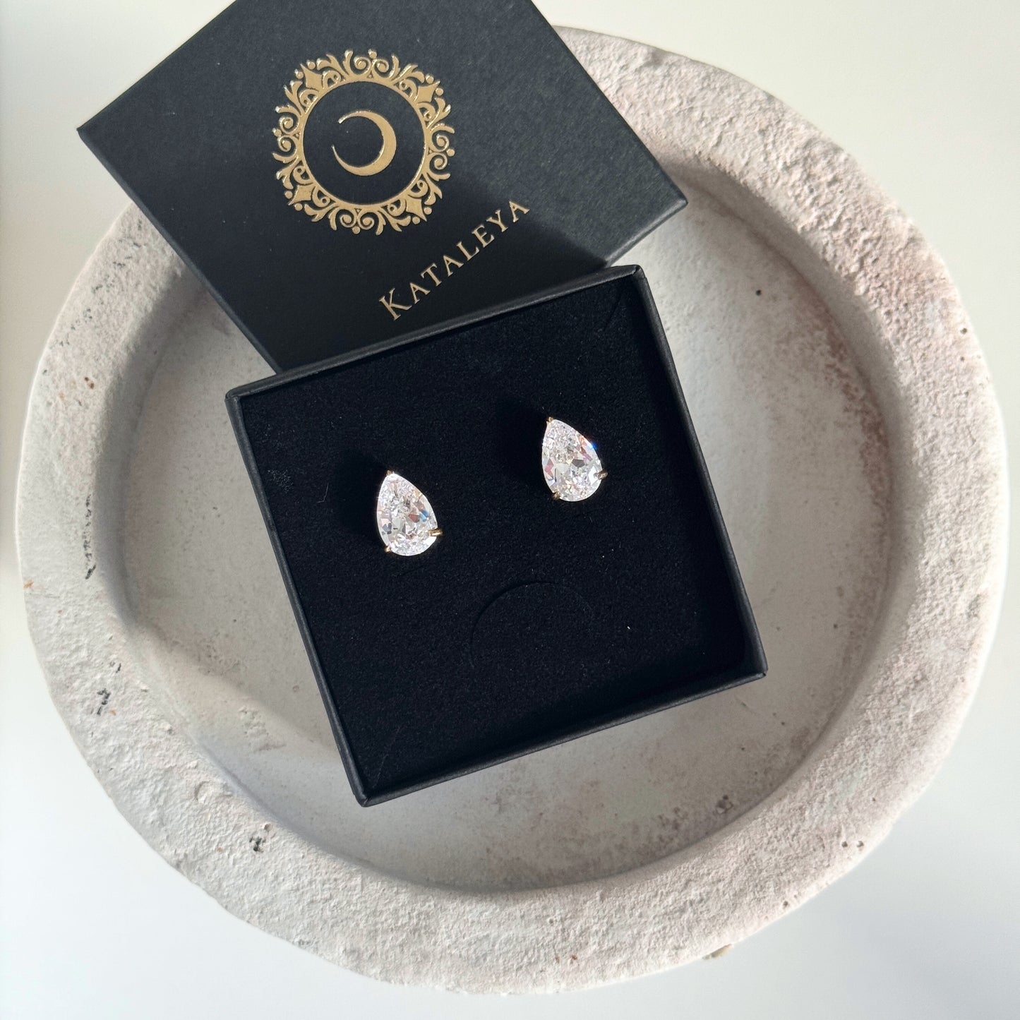 Large Teardrop CZ Stud Earrings displayed in a black box on a decorative plate.
