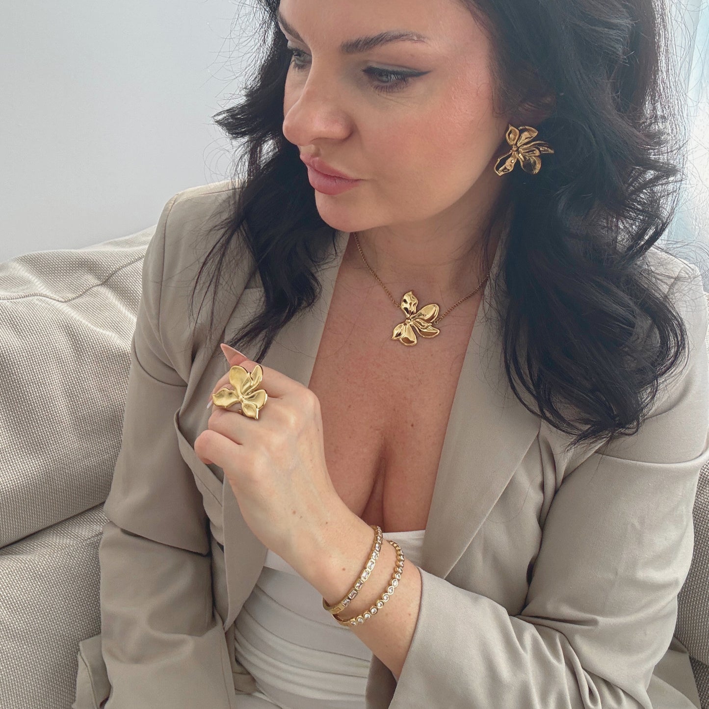 Woman wearing gold floral jewelry, including a ring and earrings, complemented by a gold zircon bangle.
