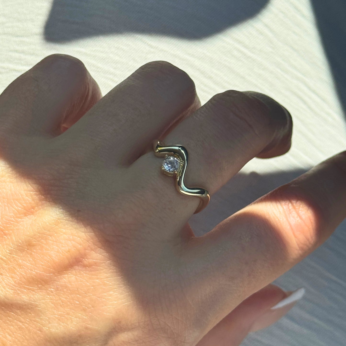 Gold Wavy Ring with a diamond on a person's finger against a light background by Kataleya Jewellery