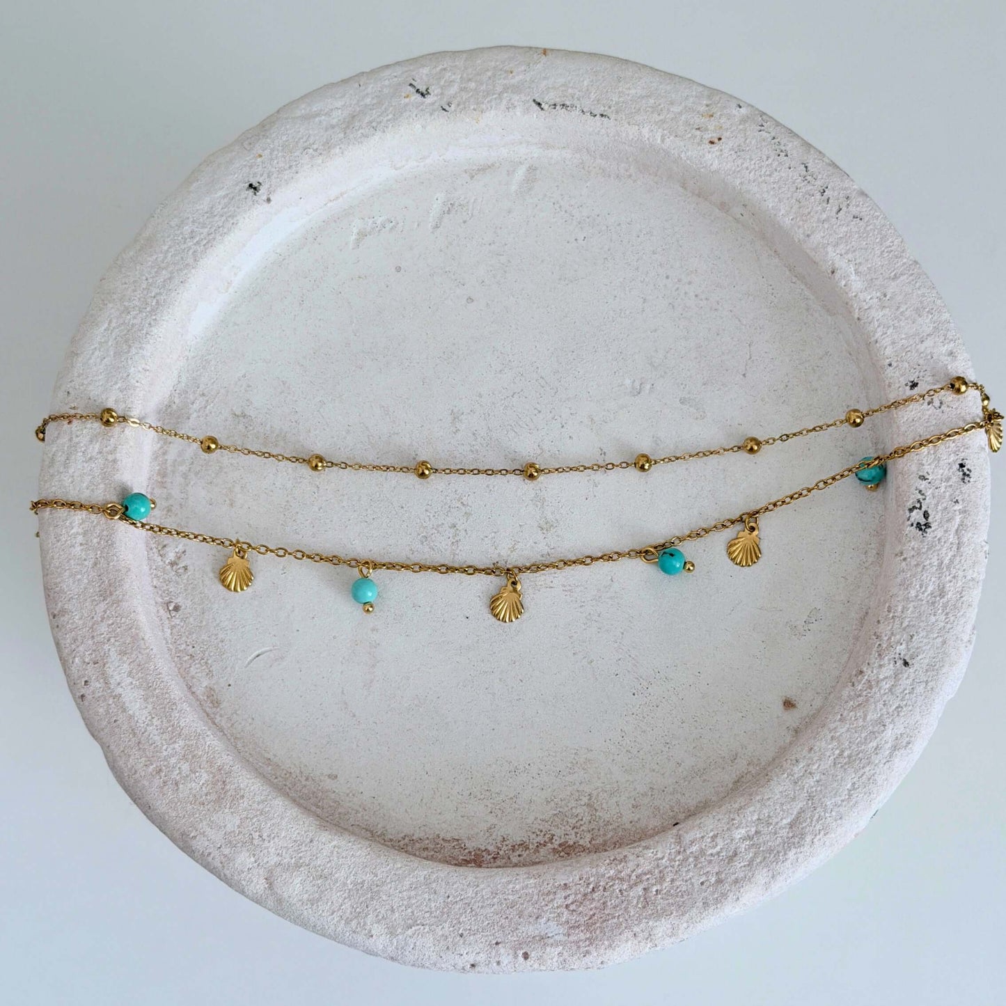 Gold Turquoise Shell Anklet displayed on a textured plate, featuring turquoise beads and shell charms.