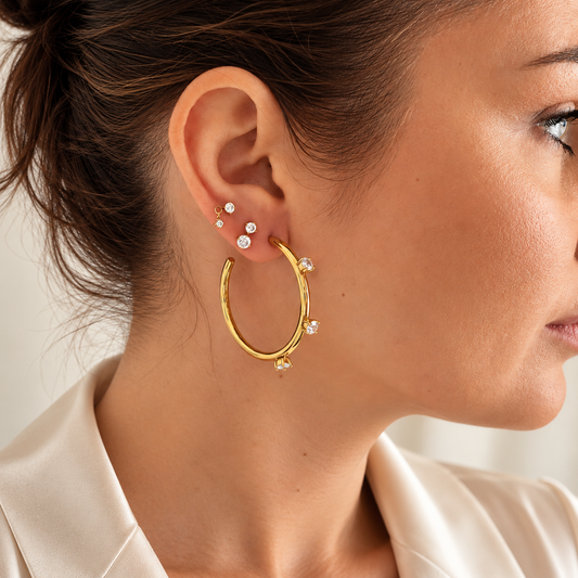 Close-up of a woman wearing Callisto Crystal Hoops, gold plated earrings featuring round crystals, showcasing elegant jewelry.