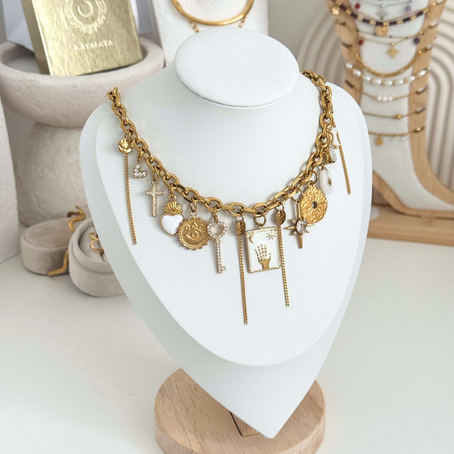 Gold necklace with charms on a white heart-shaped stand by Kataleya Jewellery