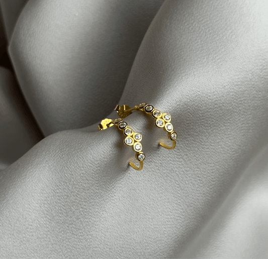 Elegant Mayach Half Hoop Earrings in 18k gold-plated sterling silver with zirconia stones on a soft fabric background.