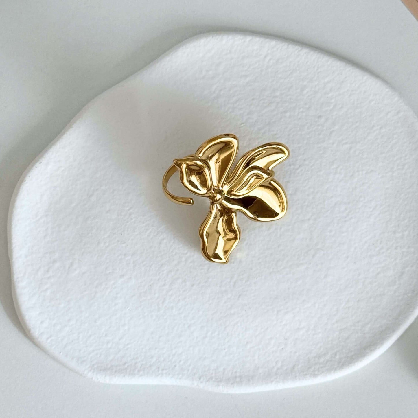 Gold Flower Jewelry ring on a white ceramic plate, showcasing its floral design and shiny finish.