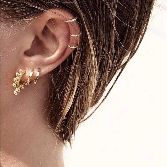 Close-up of a woman's ear featuring multiple gold earrings including a triple ear cuff and stylish hoop earrings.
