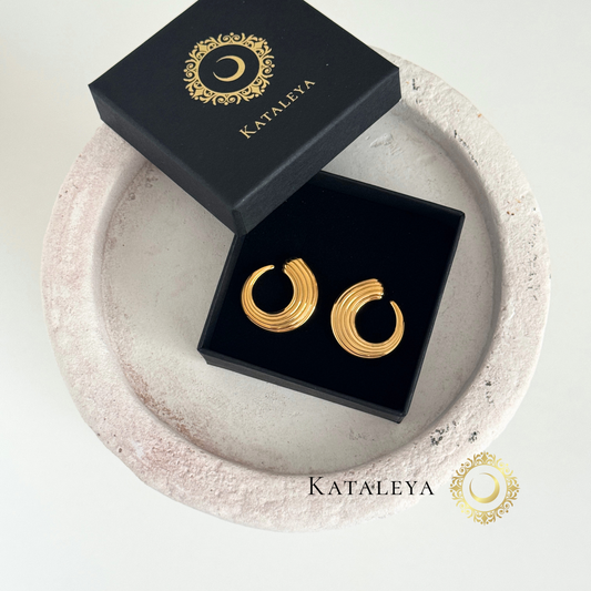 Wave Texture Hoops in a black jewelry box, featuring sculpted gold plated stainless steel design on a textured stone background.