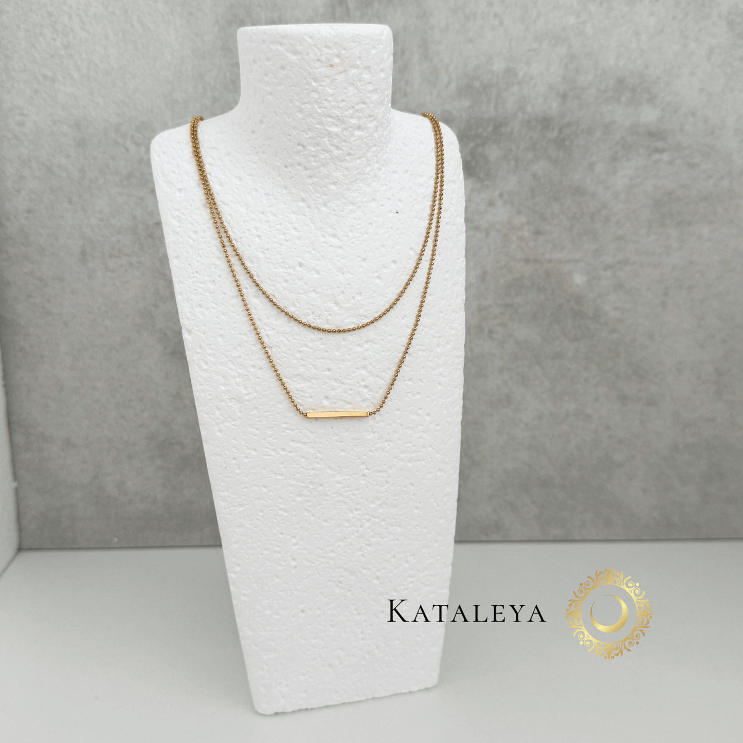 Layered Bar Necklace displayed on a white bust, featuring two gold chains and a sleek horizontal bar pendant.