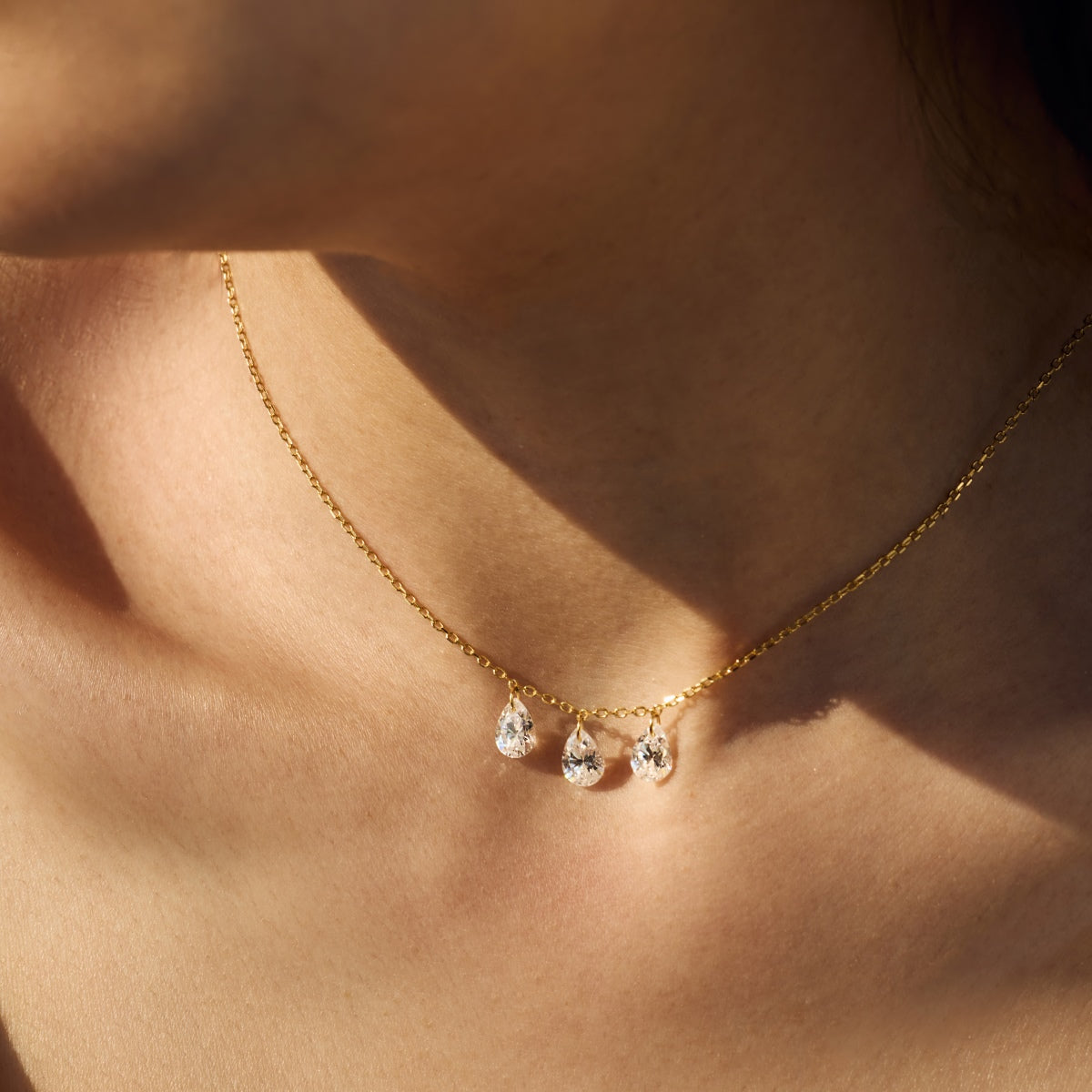 Gold Seraphine Trinity necklace with teardrop-shaped pendants on a person's neck - Kataleya Jewellery
