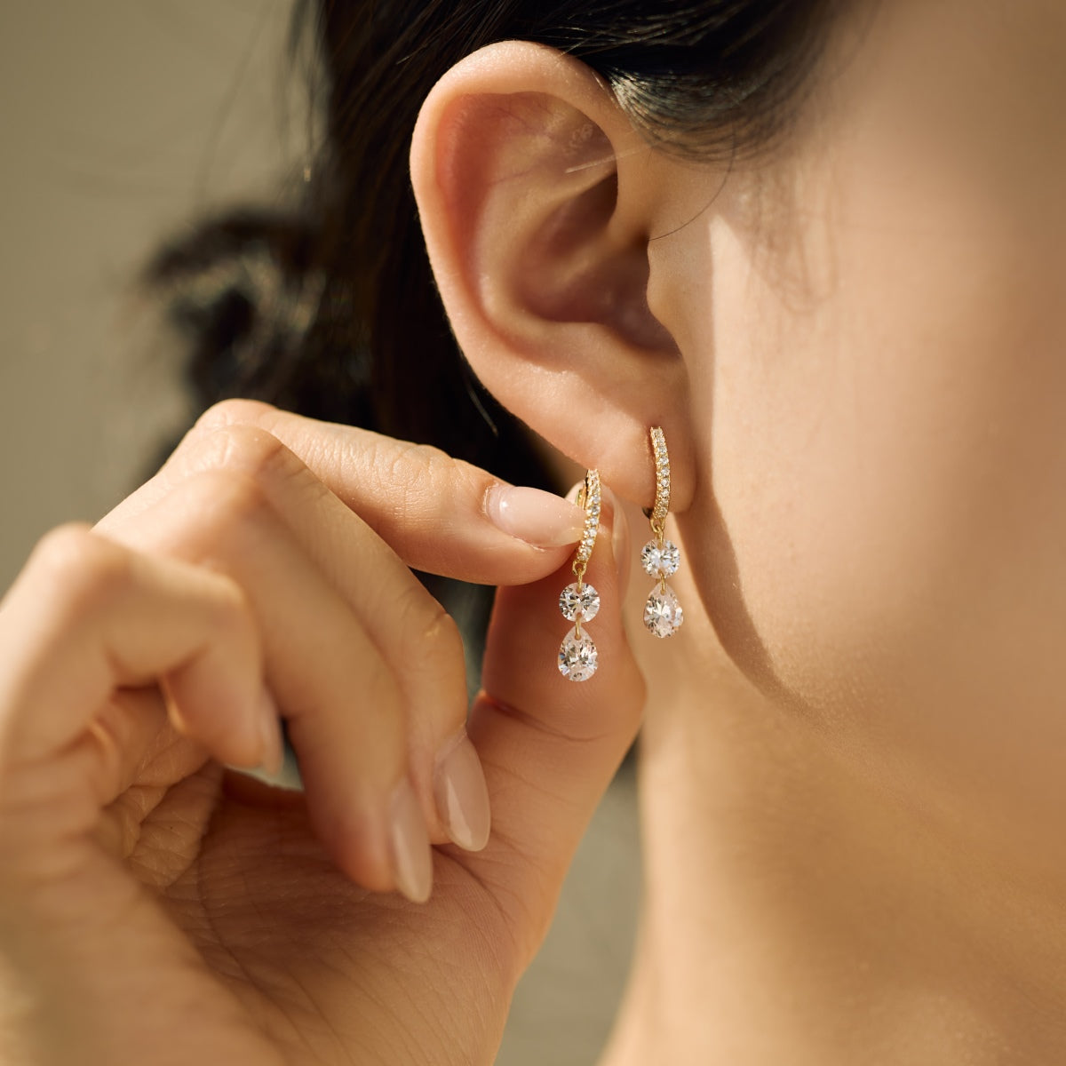 Close-up of an ear wearing a dangling hoop Seraphine Grace Earring featuring two Zircon drops with a blurred background by Kataleya Jewellery
