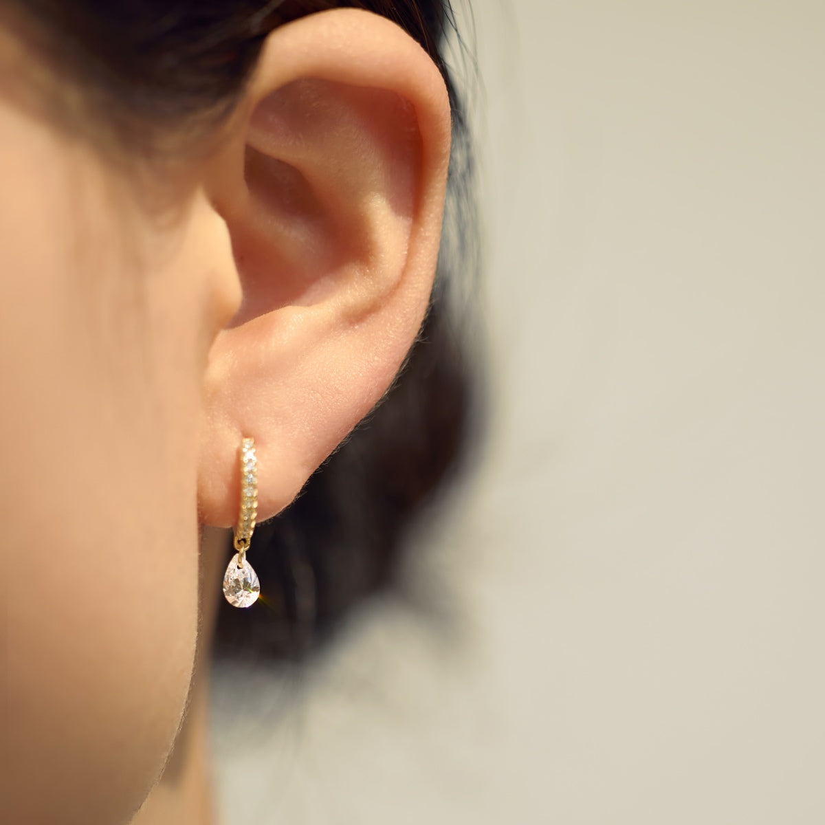 Close-up of an ear wearing a gold Seraphine Halo earring with a clear gemstone on a neutral background - by Kataleya Jewellery