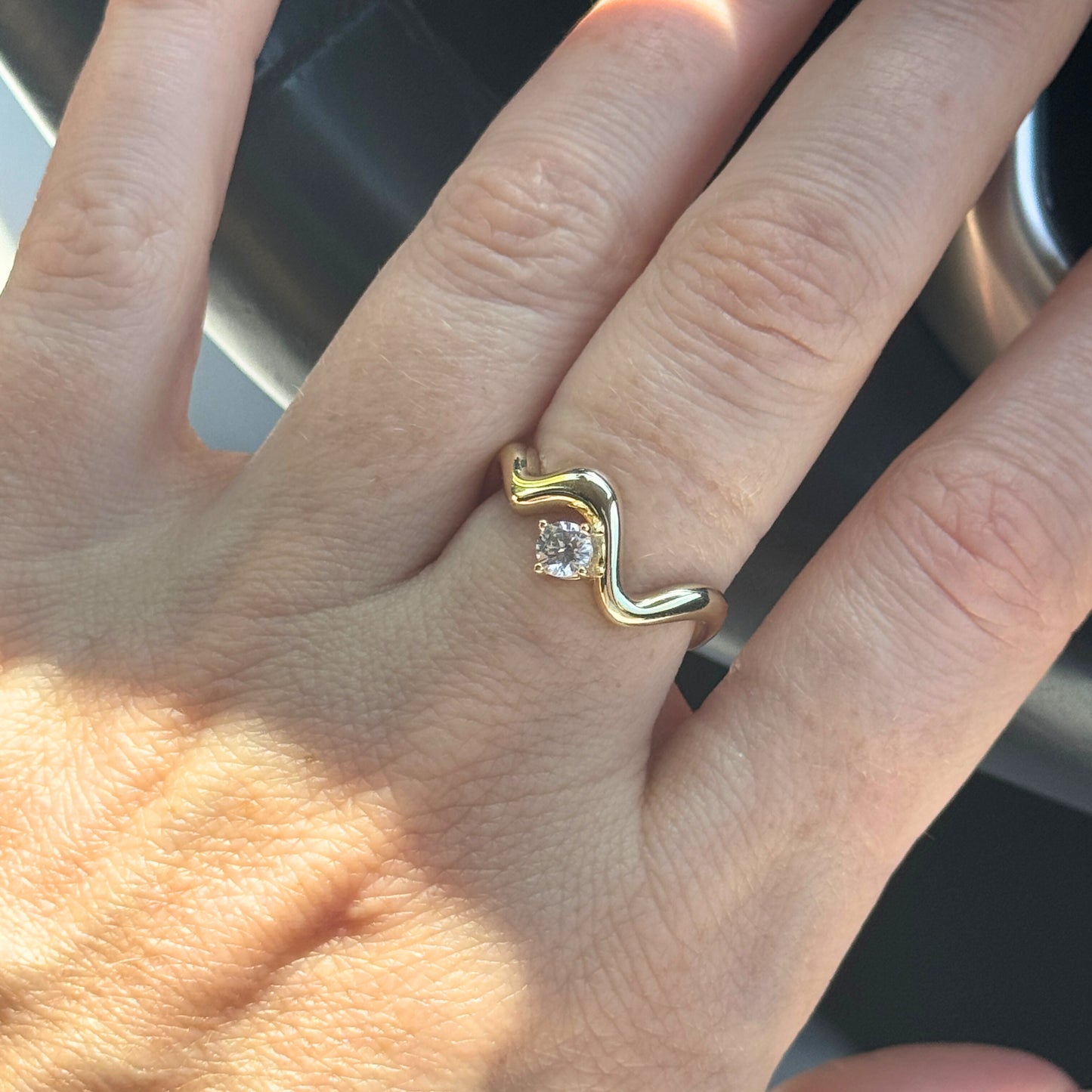 Gold wavy ring with a diamond on a person's finger by Kataleya Jewellery