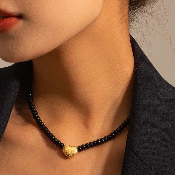 Close-up of a beaded heart necklace with a gold pendant, worn on a model's neck, showcasing elegance and style.