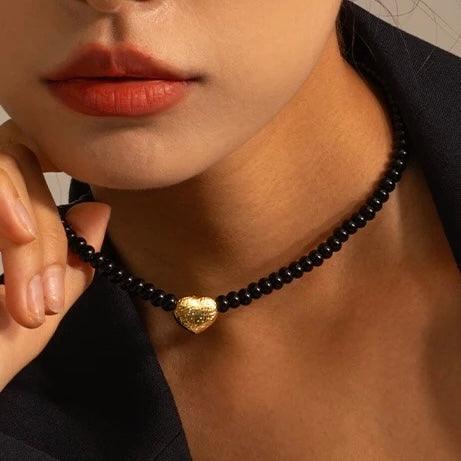 Close-up of a woman wearing a beaded heart necklace with a gold pendant and black beads, showcasing elegance and style.
