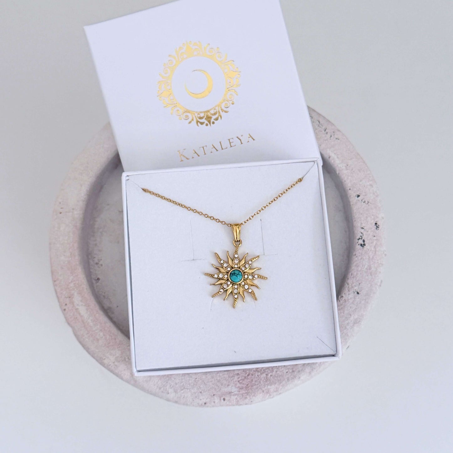 Nera Sun Necklace | Turquoise Sun Pendant Necklace displayed in a jewelry box with a gold sun pendant and turquoise stone.