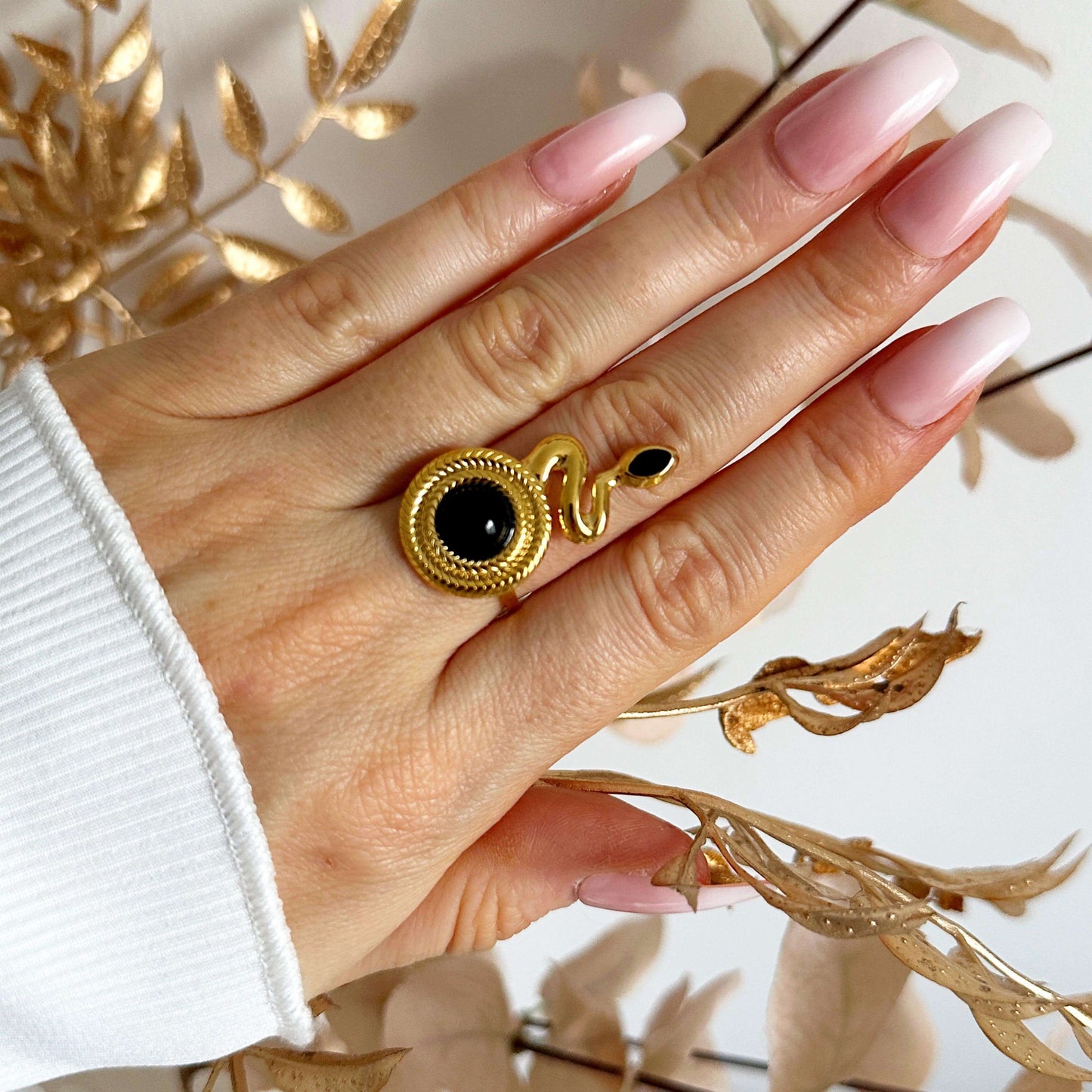 Stylish hand wearing a chic gold plated Snake Agate ring with black agate stone, complementing long pink nails.