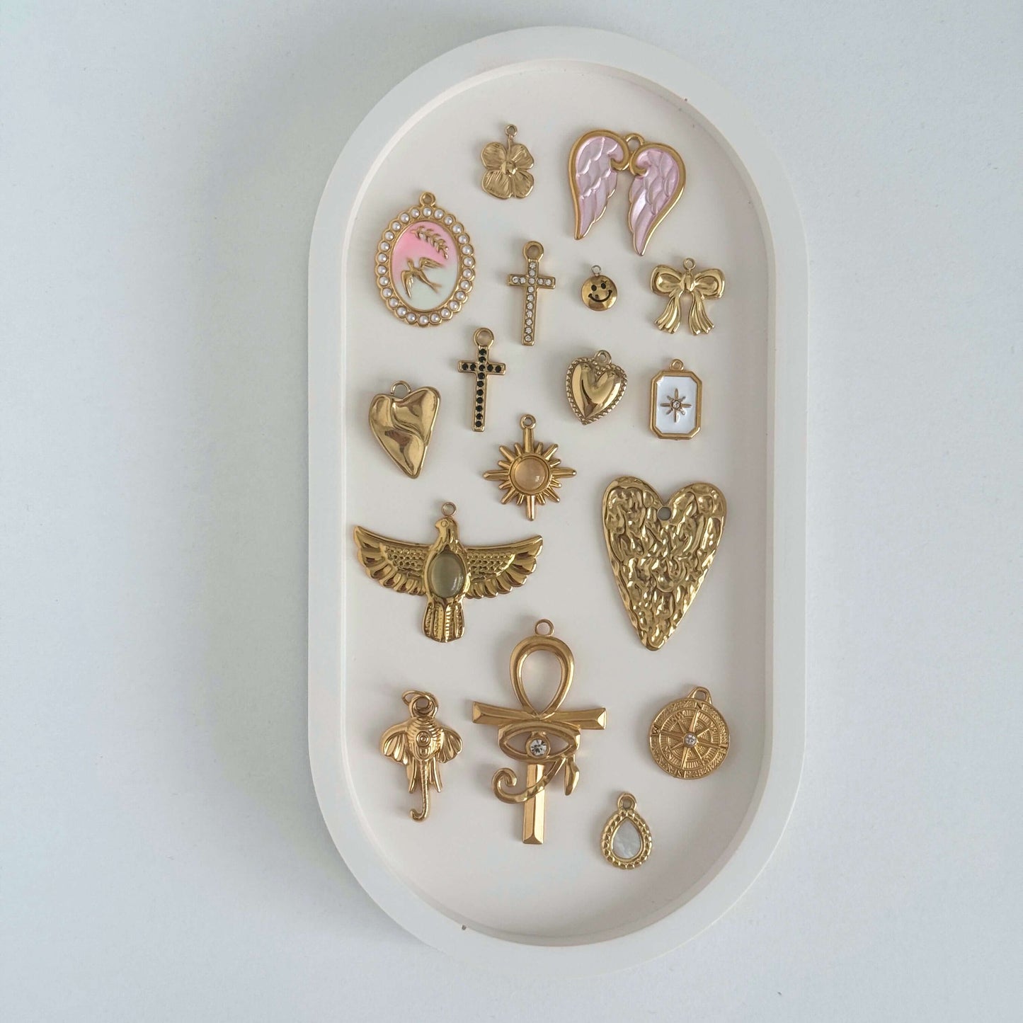 A collection of various gold charms including angels, crosses, and hearts displayed in an oval tray.