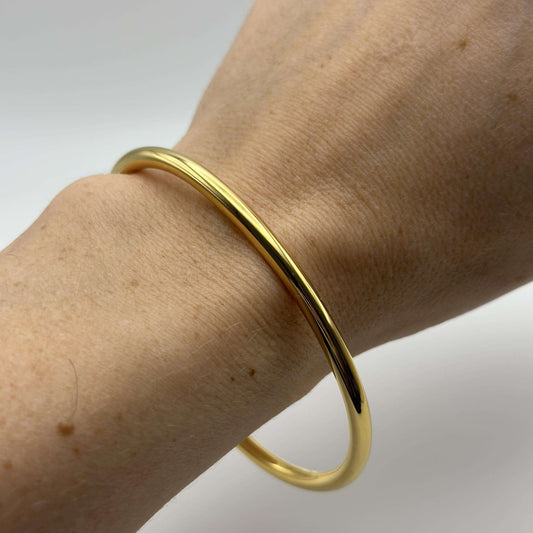 Close-up of a hand wearing a gold open bangle made from 18k gold plated stainless steel.