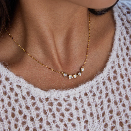 Heart Tennis Chain Necklace featuring five heart-shaped cubic zirconia stones, elegantly worn on a delicate gold chain.