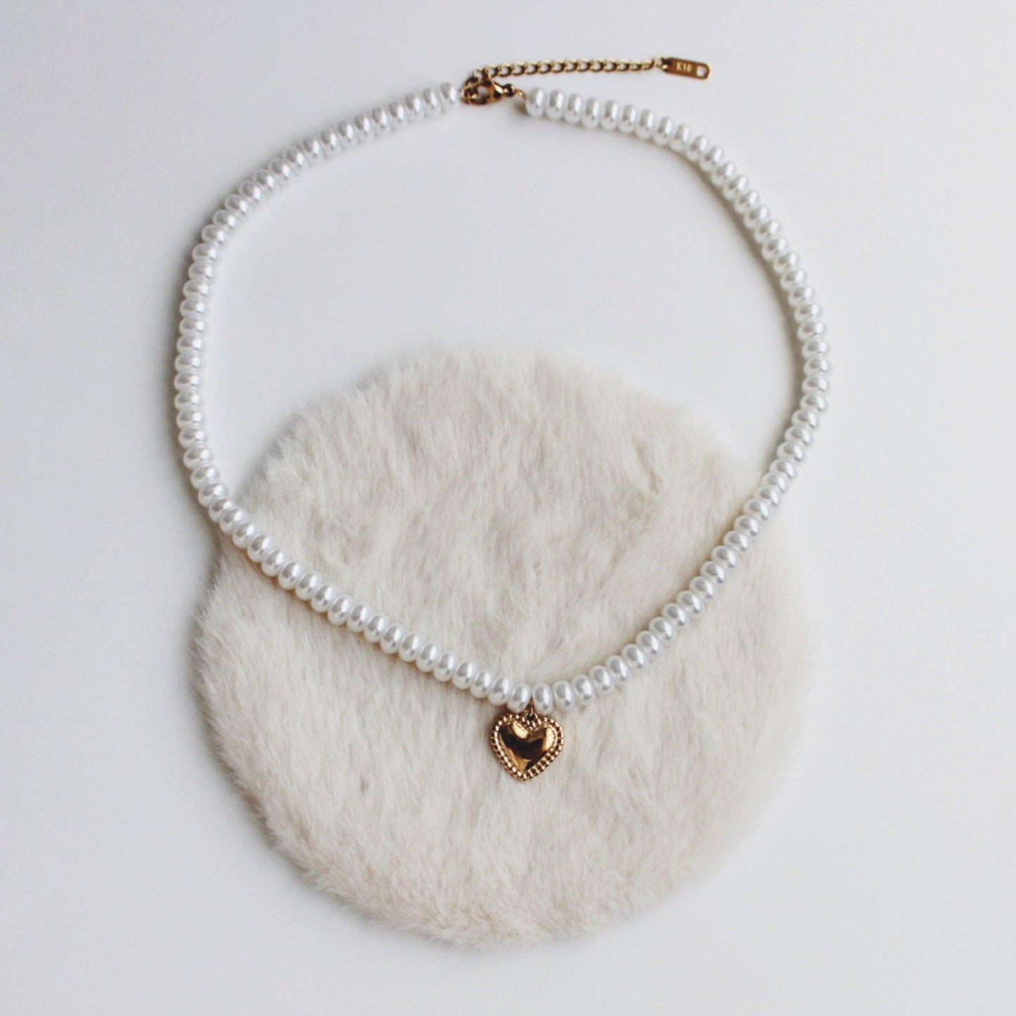 Elegant heart pearl necklace with a gold pendant on a soft fur background.