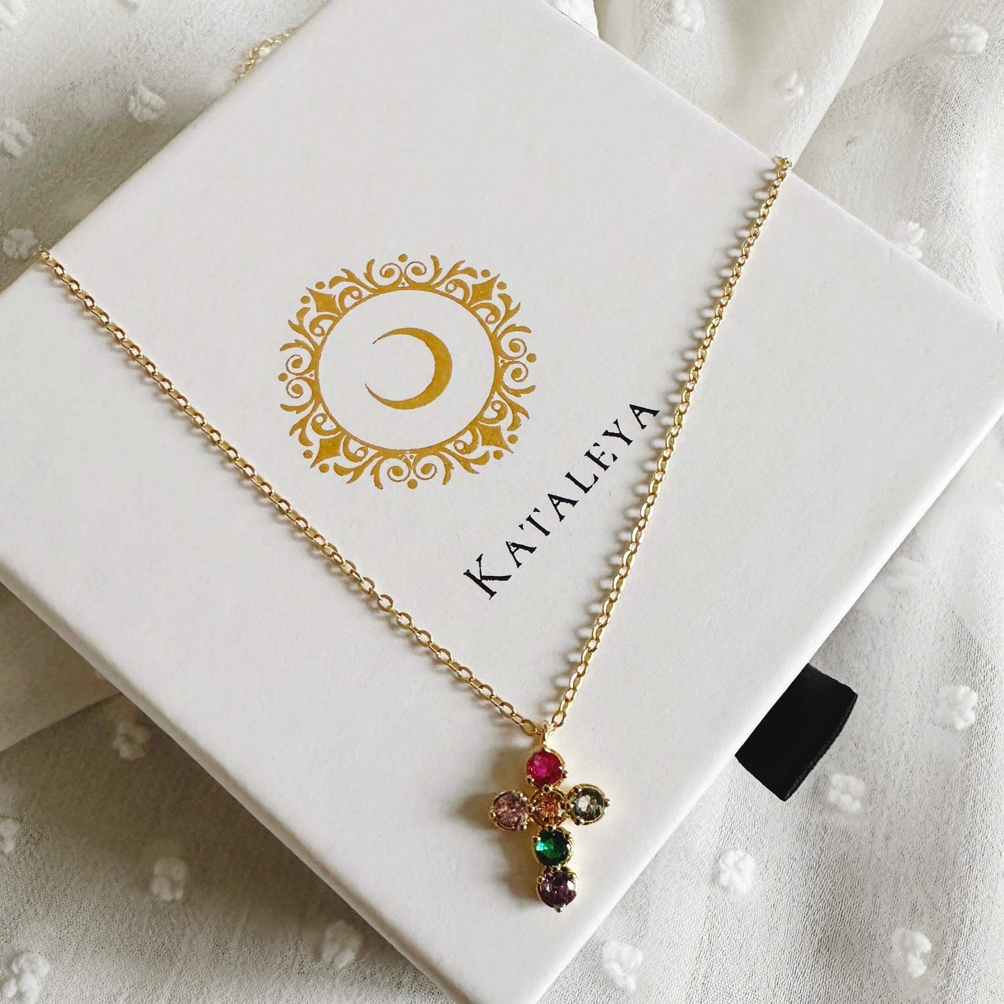 Leilani Cross necklace displayed in a Kataleya box with colorful zircon stones on a gold chain.
