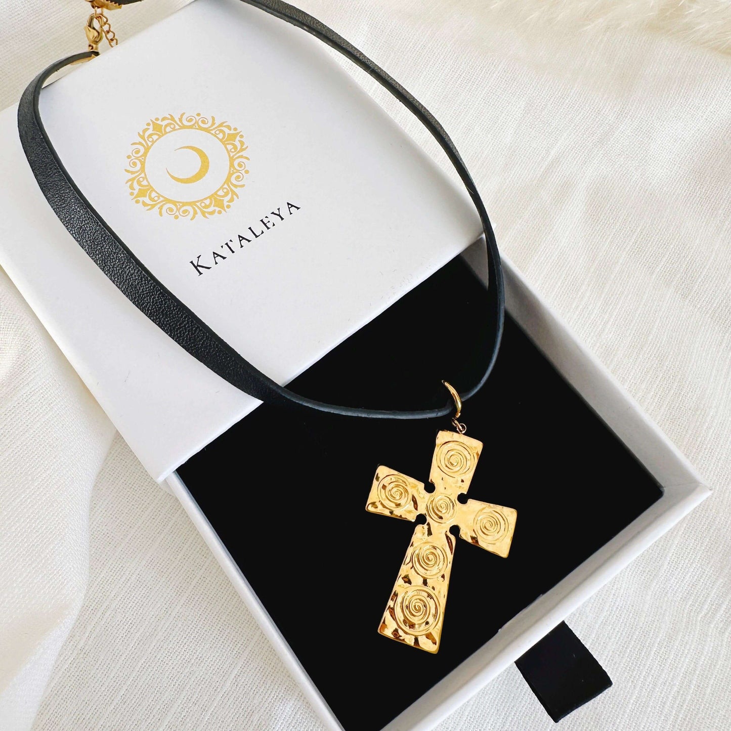 Gold cross pendant on a black leather choker presented in a stylish jewelry box.
