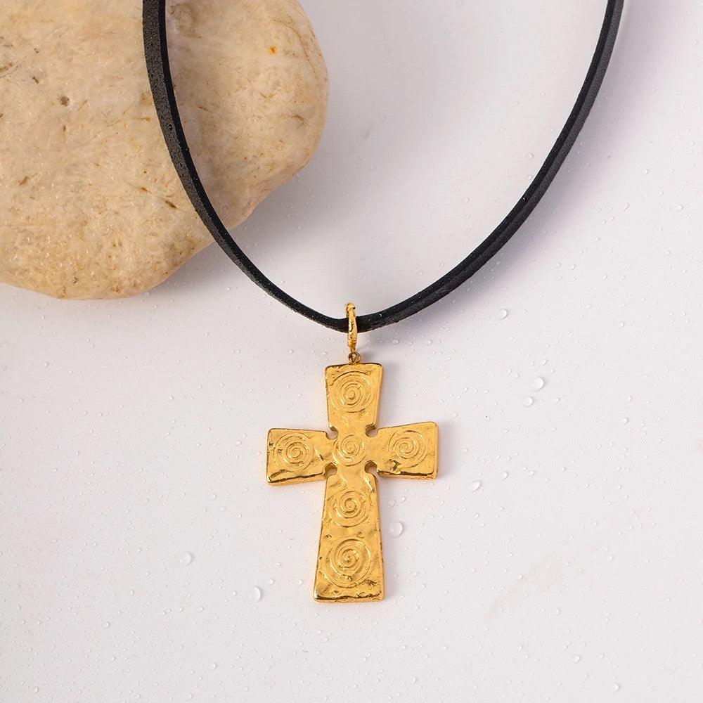 Gold cross pendant on a black leather choker resting on a light stone surface, showcasing a stylish jewelry piece.