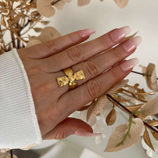 Stylish hand wearing a Cross Gold Ring, showcasing its shiny gold finish against a backdrop of neutral decor.