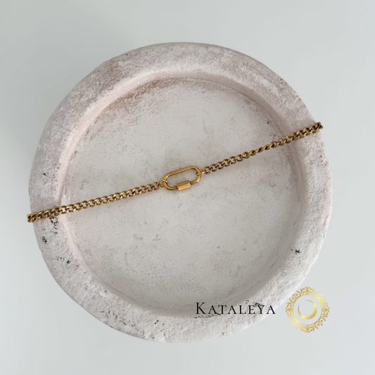 Oval Carabiner Charm Necklace resting on a decorative dish, showcasing its waterproof and tarnish-free gold finish.