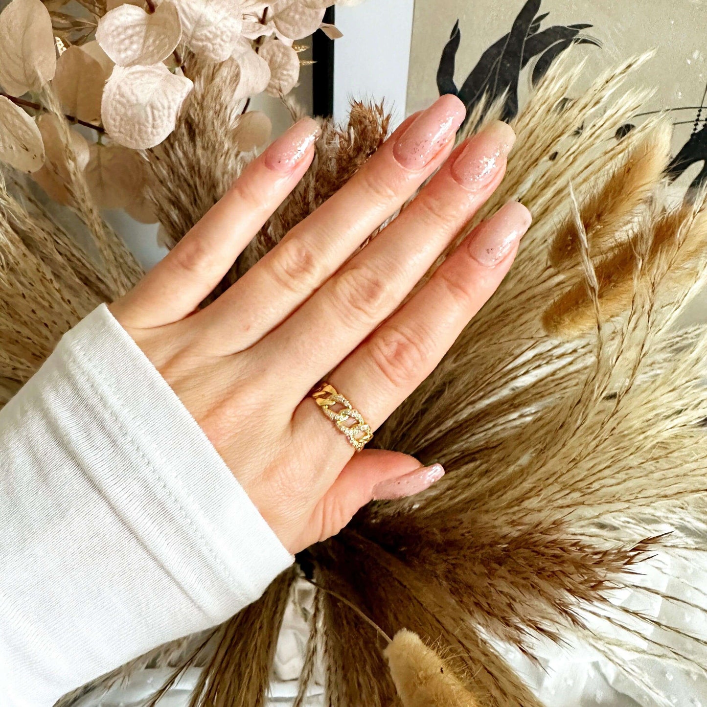 Woman showcasing a gold-plated ring against a backdrop of dried floral arrangements.