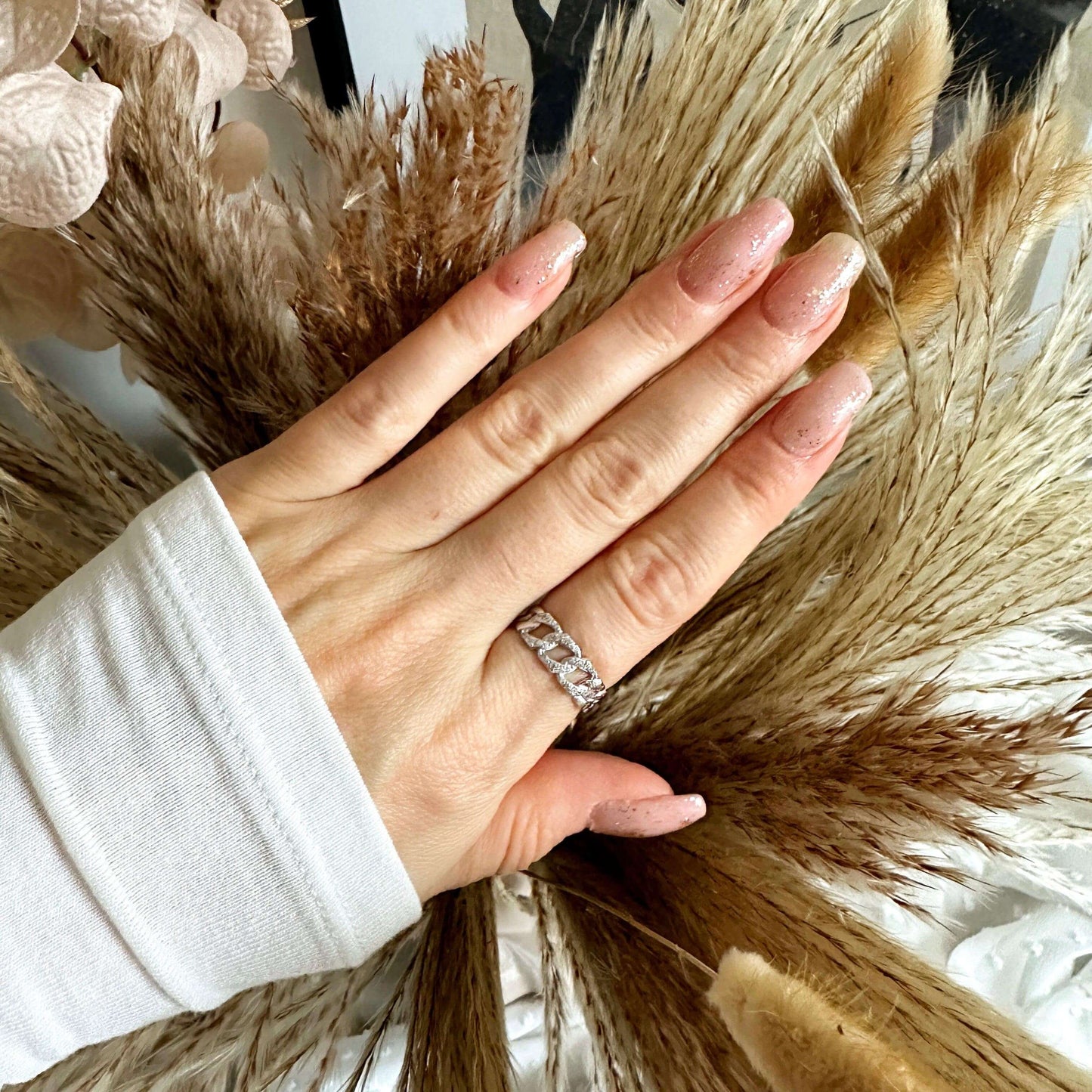 Hand adorned with a sparkling silver ring, resting on a backdrop of dried floral arrangements.