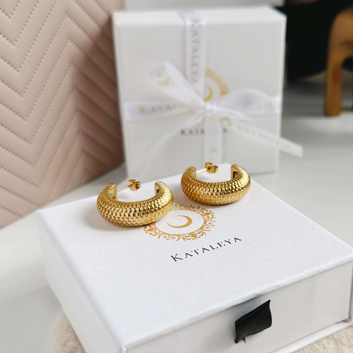 Chunky gold hoop earrings with a snake design displayed on a gift box.