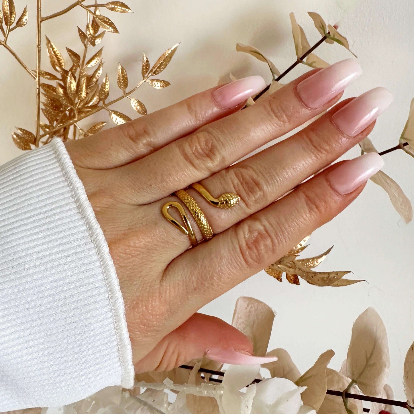 Hand wearing a stylish gold snake ring with a slithering design, complemented by elegant acrylic nails.