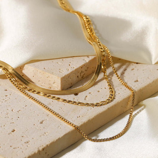 Goddess Layers Necklace showcasing three gold chains on a textured surface.