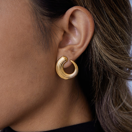 Close-up of a woman wearing Wave Texture Hoops, waterproof gold-plated stainless steel earrings with a wave design.