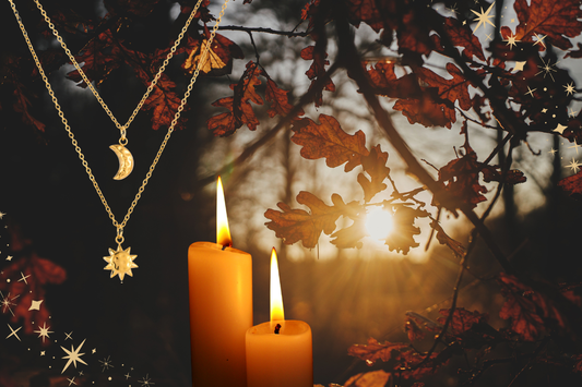 Gold sun and moon pendant necklaces with lit candles and autumn leaves at sunset