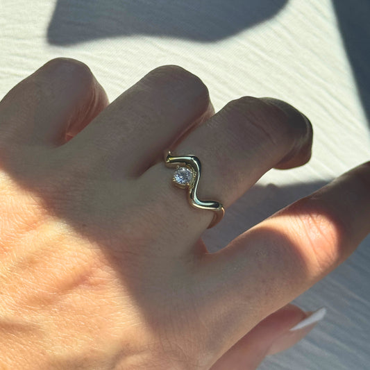 Gold Wavy Ring with a diamond on a person's finger against a light background by Kataleya Jewellery 