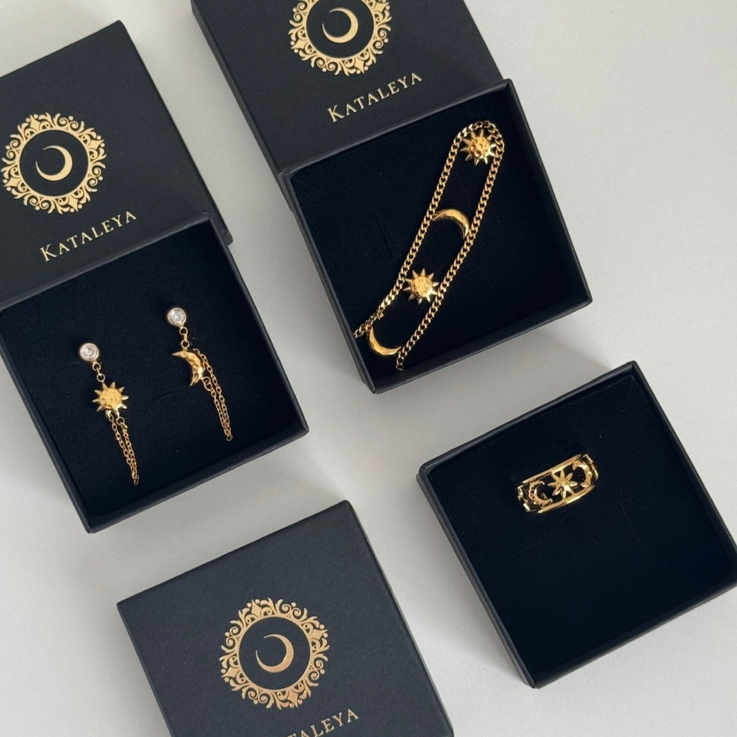 Gold sun & moon jewelry set in black boxes with 'Kataleya' branding on a light gray background