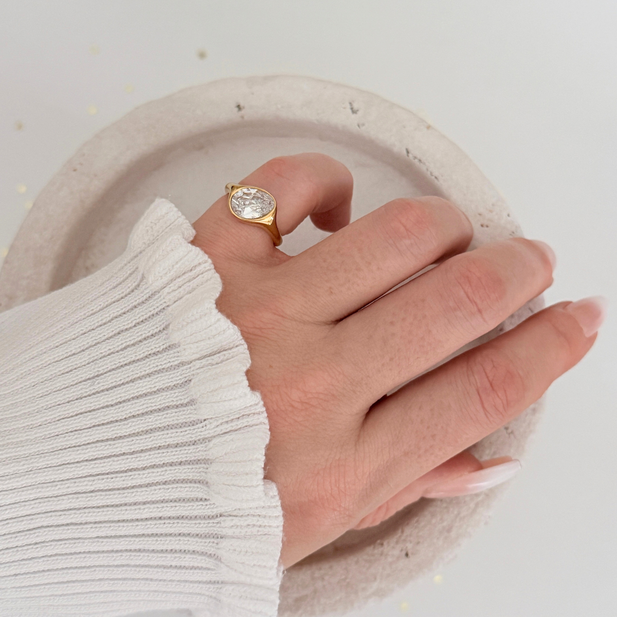 Elara Pinky Ring featuring an oval cubic zirconia set in gold, worn on a hand with a white sweater.