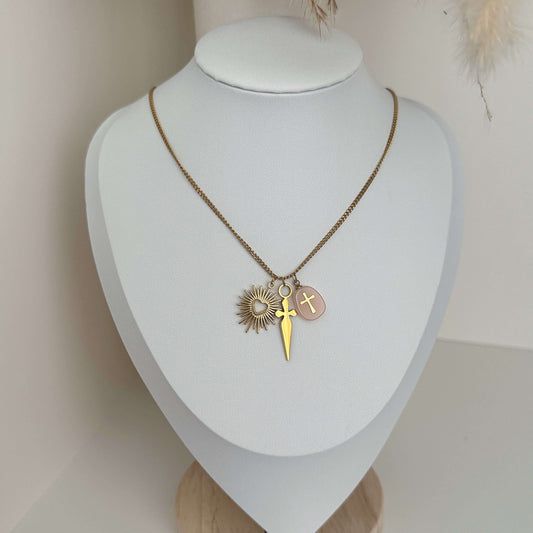 Golden Trinity Charm Necklace featuring a sunburst, a dagger, and a gold cross on a pink stone - Kataleya.