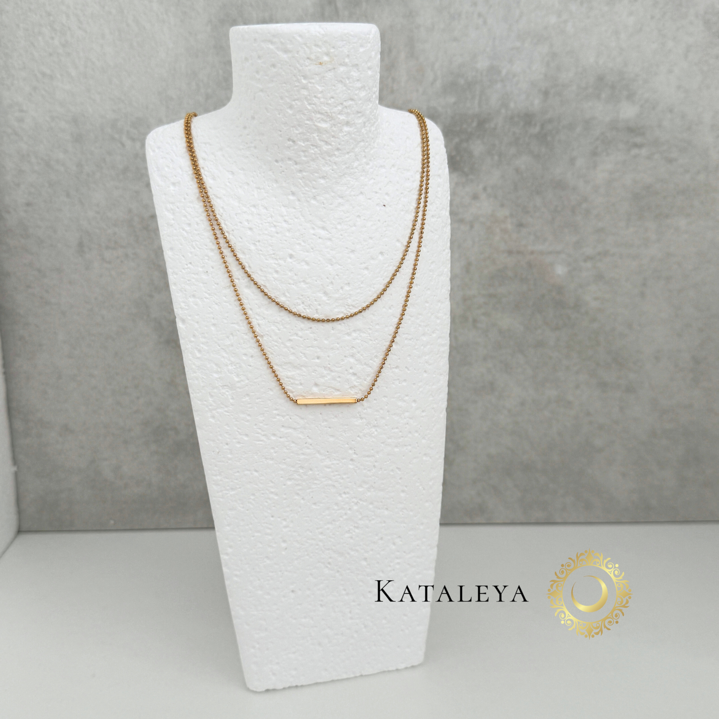 Layered Bar Necklace displayed on a white bust, featuring two gold chains and a sleek horizontal bar pendant.