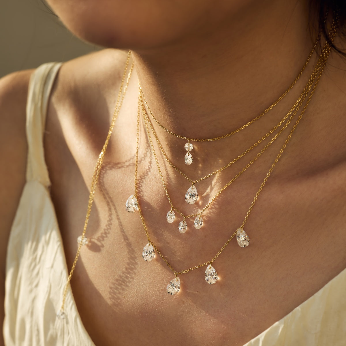 Close-up of a person wearing gold necklaces with teardrop-shaped pendants - Kataleya Jewellery
