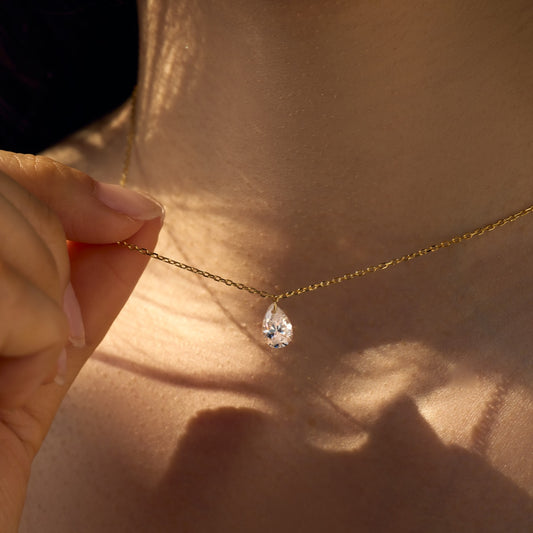 Gold Seraphine Halo necklace with a teardrop-shaped pendant held against a person's neck - Kataleya Jewellery