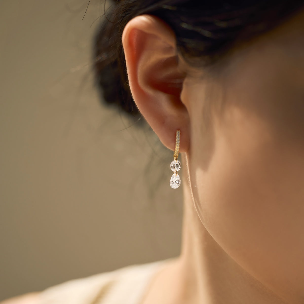 Close-up of an ear wearing a dangling hoop Seraphine Grace Earring featuring two Zircon drops with a blurred background by Kataleya Jewellery