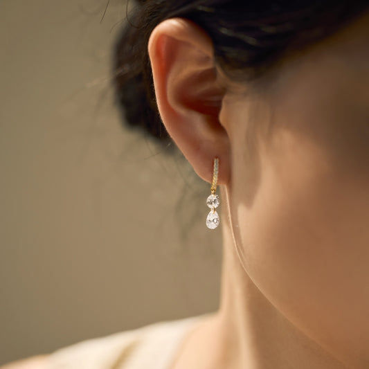 Close-up of an ear wearing a dangling hoop Seraphine Grace Earring featuring two Zircon drops with a blurred background by Kataleya Jewellery
