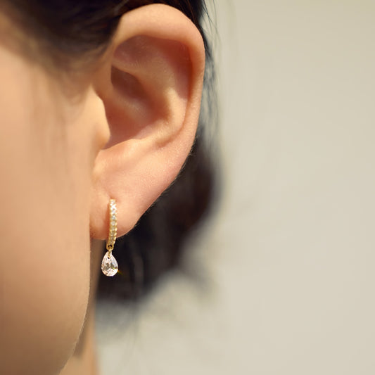 Close-up of an ear wearing a gold Seraphine Halo earring with a clear gemstone on a neutral background - by Kataleya Jewellery
