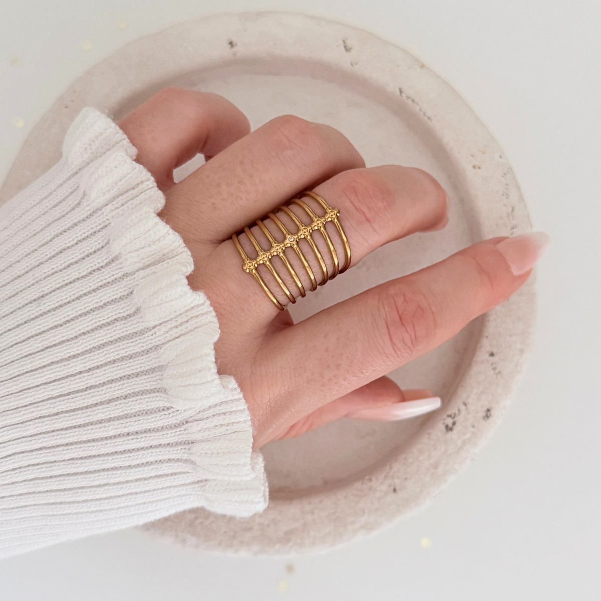 Orla Cage Ring showcased on a hand with gold bands and cubic zirconia, styled on a pink dish.