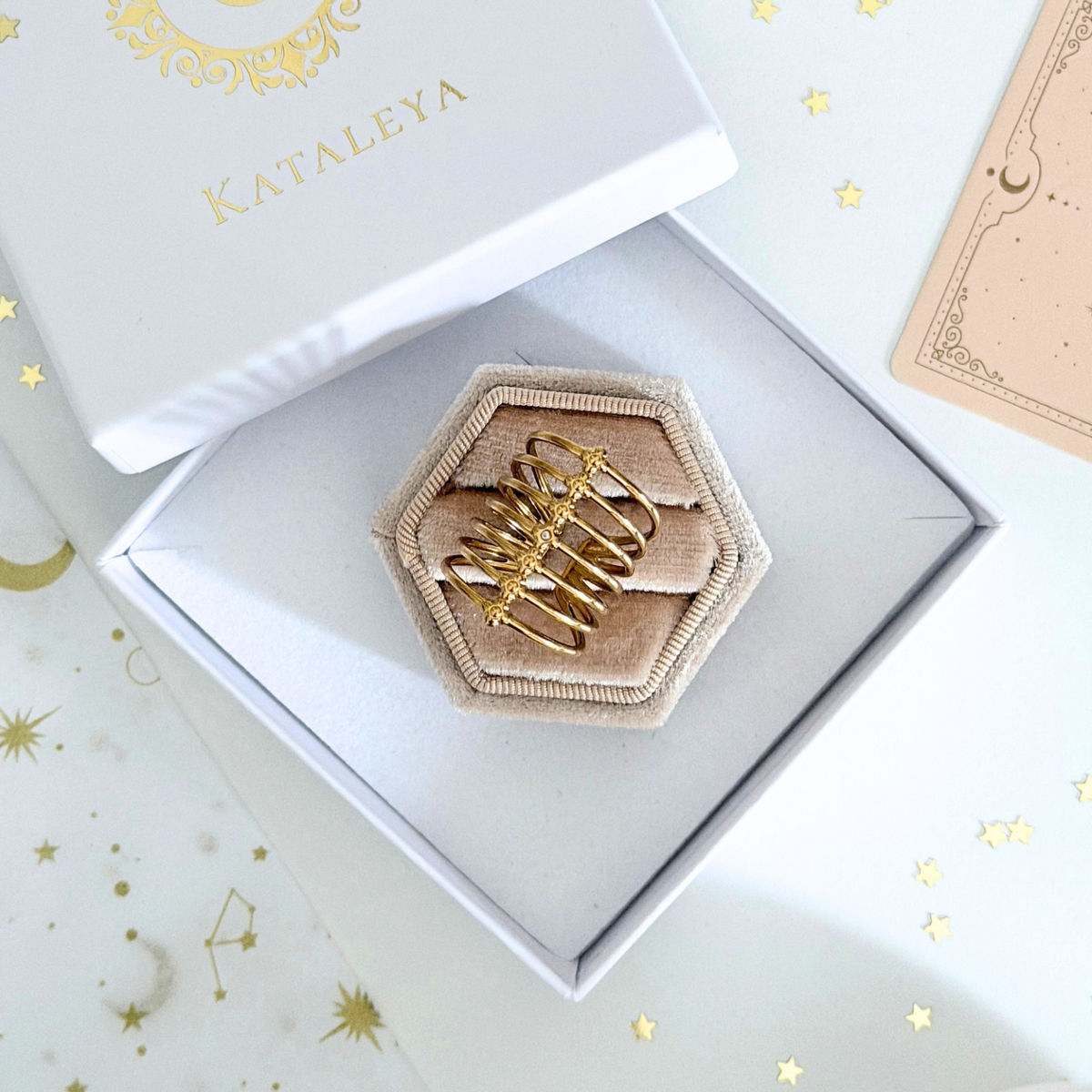 Orla Cage Ring displayed in a hexagon ring box with a soft interior, featuring fine gold bands and delicate beads.