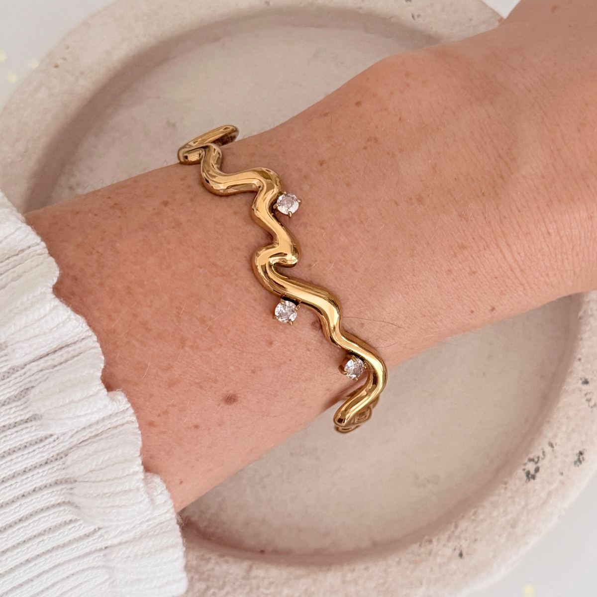 Thalia Squiggle Cuff on wrist featuring three round crystals in gold plated stainless steel.