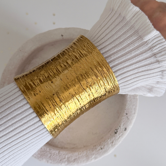 Theia Wide Cuff worn on a wrist, showcasing its textured golden surface and bold design.