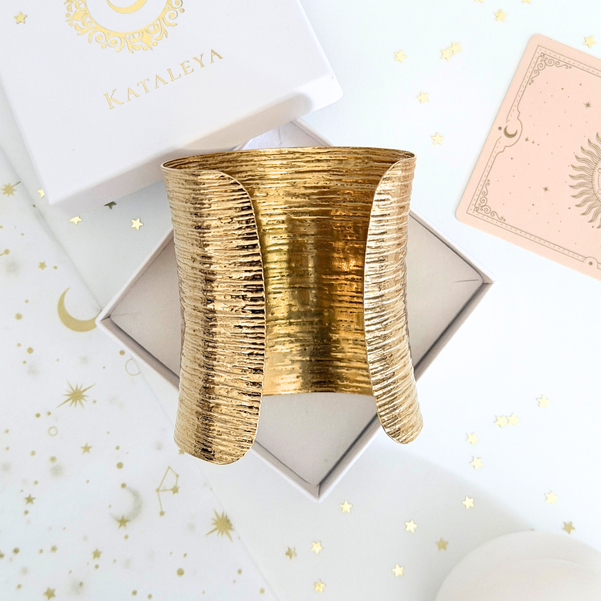 Theia Wide Cuff displayed on a gift box, featuring a unique beaten metal texture and bold design.